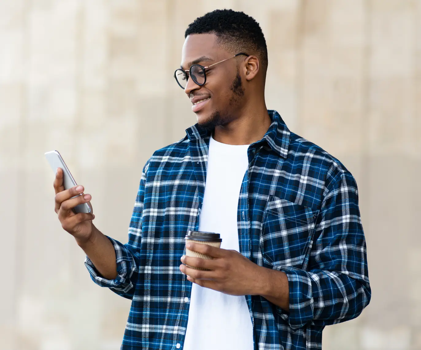 Smiling man holding a coffee and checking his phone