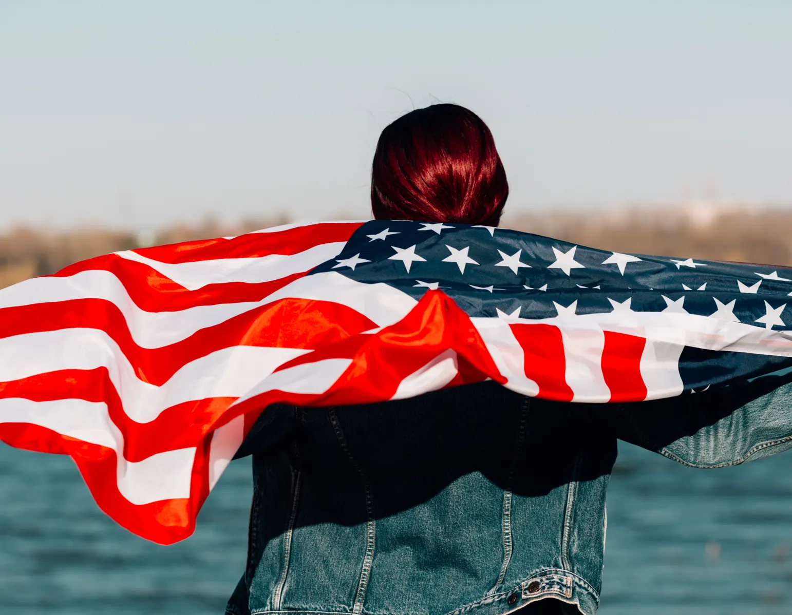 Person wrapped in an American flag by the water